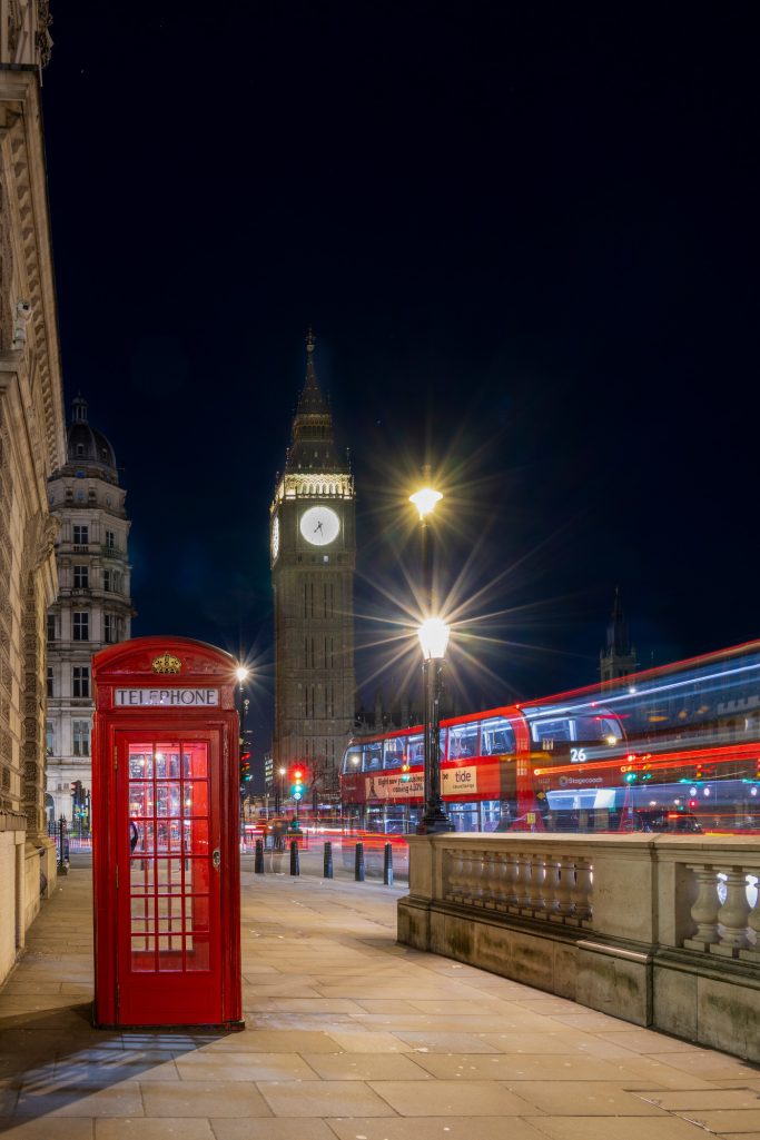 Red phone booth in front of Big Ben and an illuminated street at night.