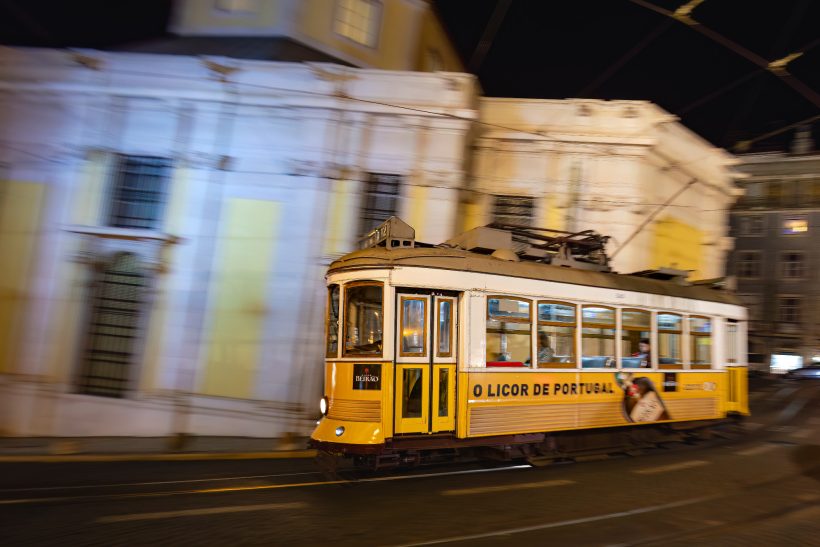 Gelbe Straßenbahn fährt bei Nacht durch eine beleuchtete Stadt.