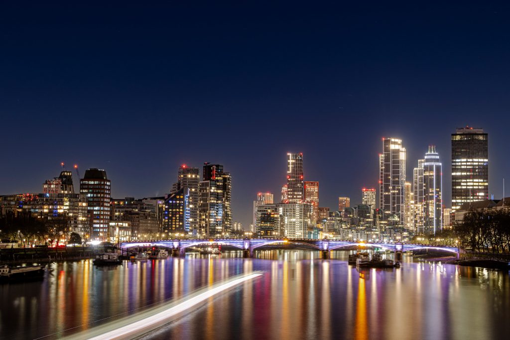 Nocturnal cityscape of London with illuminated skyscrapers and reflective water surface.