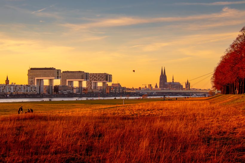 Landscape at sunset with river, historic buildings and rows of trees in the foreground.