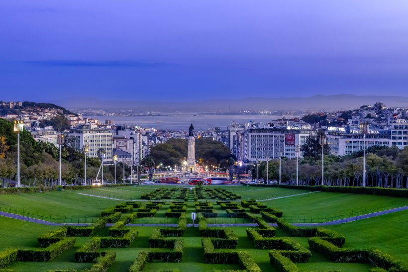 Panoramic views of a city with gardens and a monument in the foreground.