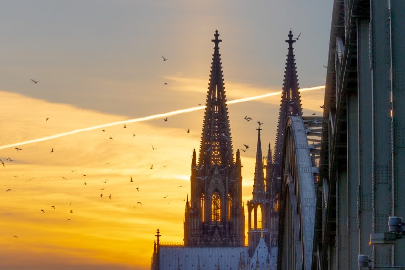 Silhouettes of church towers against a colorful sunset with a plane strip.