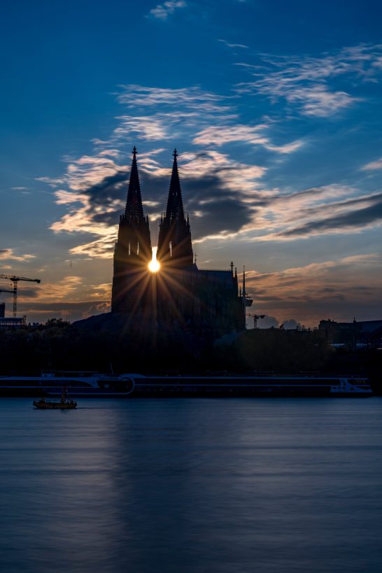 Cologne Cathedral in front of a dramatic sunset with bright light between the towers.