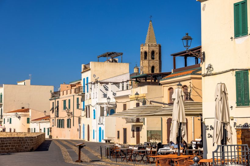 Colorful houses and cafes in a sunny square, with church tower in the background.