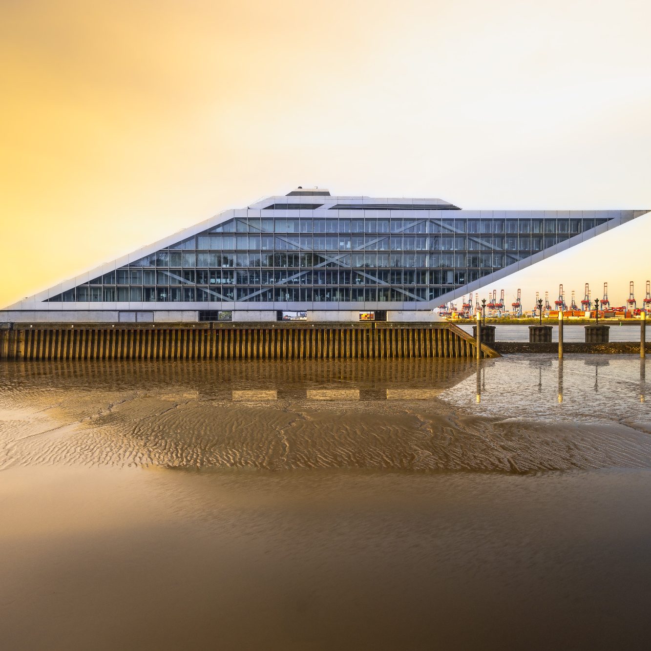 Modern architecture of a flat, triangular building by the water at sunset.