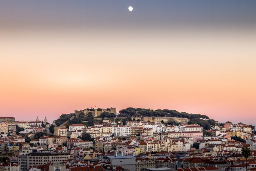 Hill with city view and moon in the sky during the twilight.