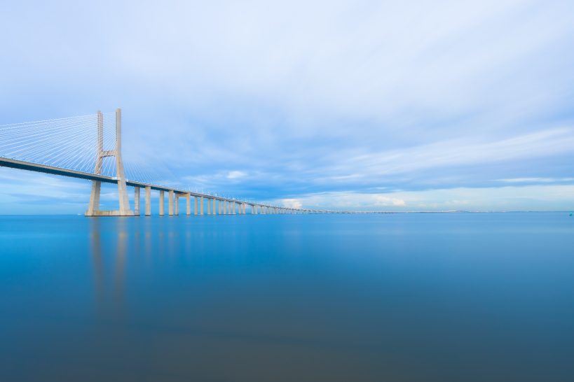 Moderne Brücke über ruhiges Wasser, umgeben von einem bewölkten Himmel.