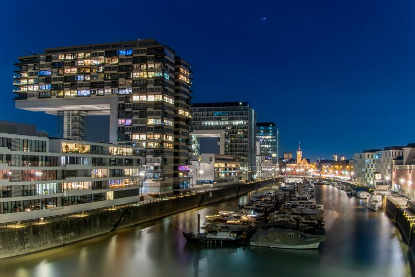 Moderne Gebäude am Hafen bei Nacht, beleuchtet und spiegelnd im Wasser.