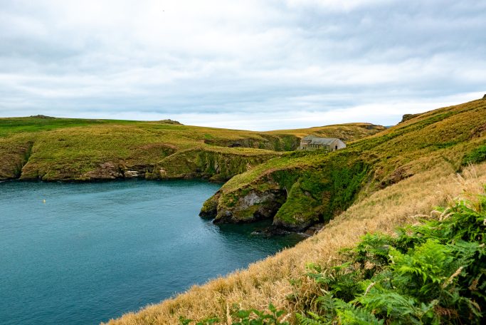 Coastal landscape with green hills, rolling waves and cloudy sky.