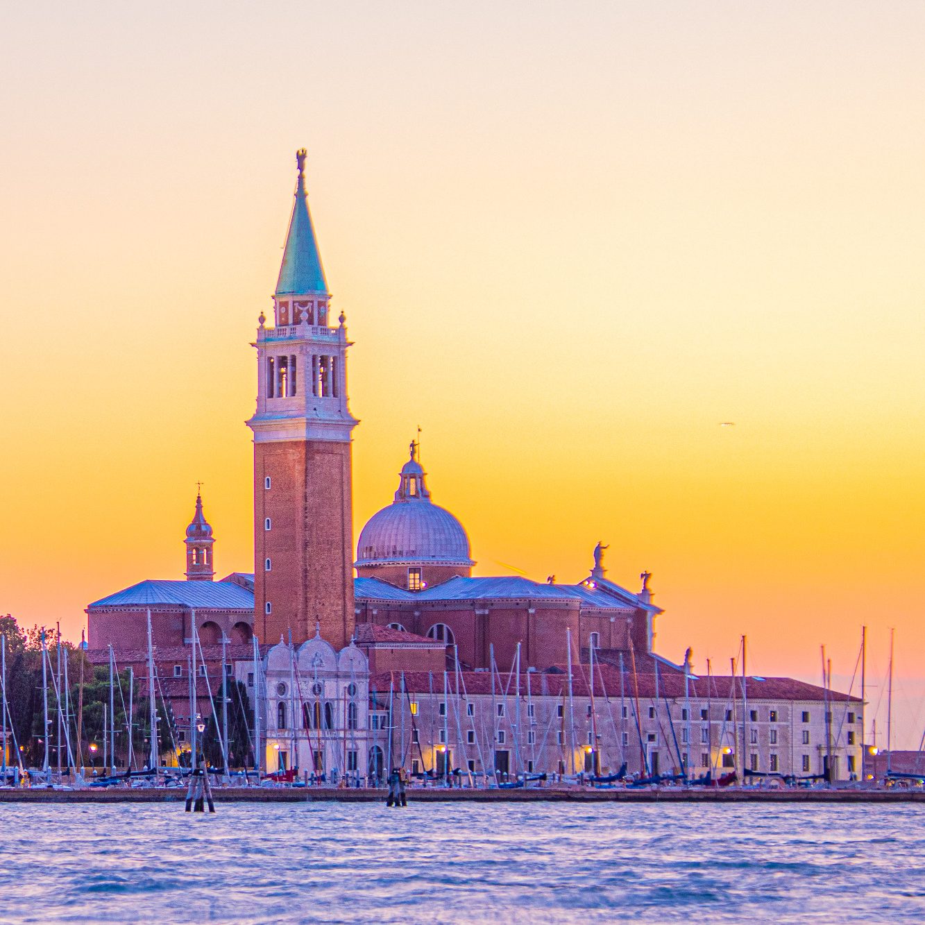 Venetian architecture with a tower and a dome in front of anunsetian sky.