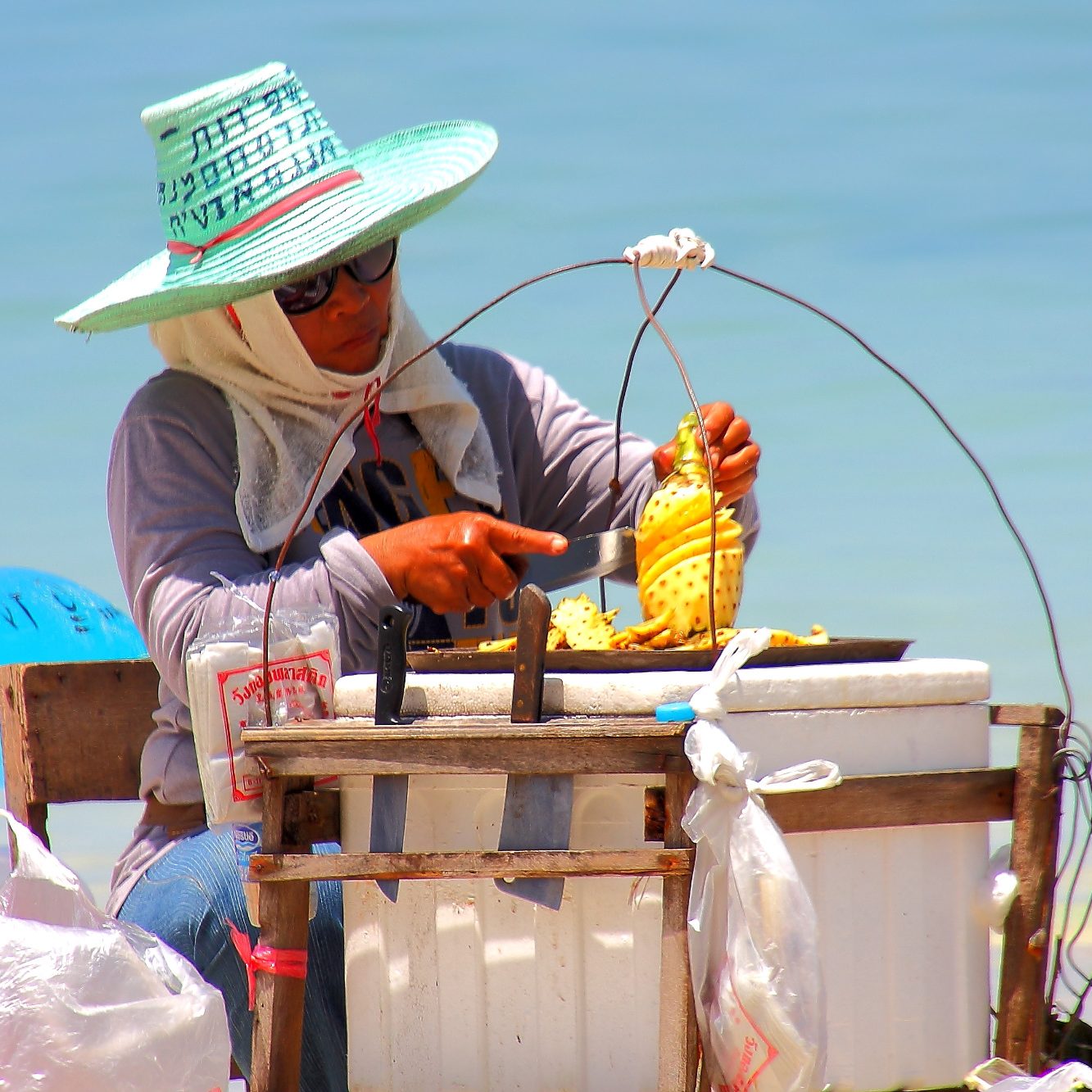 A person in a hat prepares dishes on the beach.