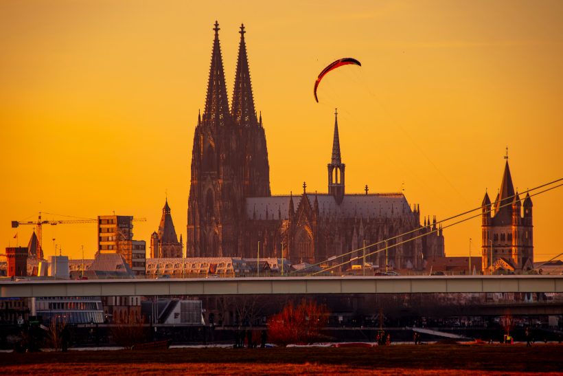 Paraglider schwebt vor der silhouette des Kölner Doms bei Sonnenuntergang.