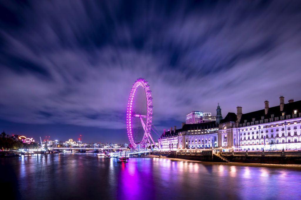 Ferris wheel in London's night light, surrounded by clouds and the Thames.