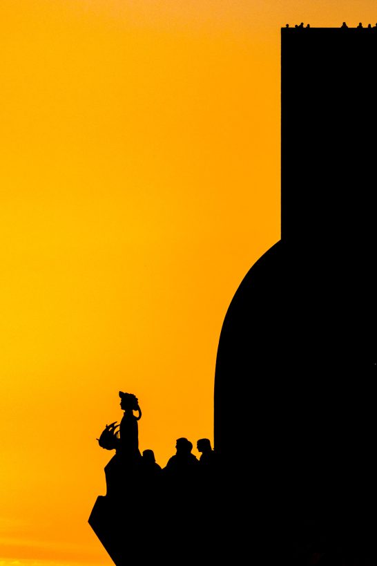 Silhouettes of people in front of an orange sky at sunset.