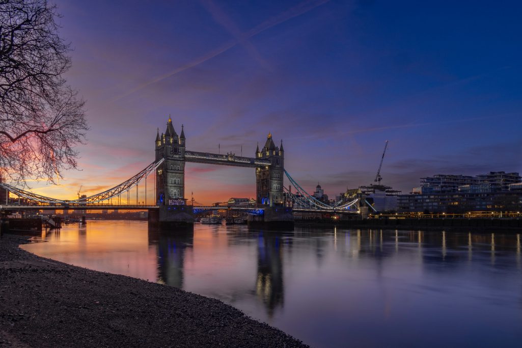 Die Tower Bridge bei Sonnenaufgang, reflektiert im ruhigen Wasser.