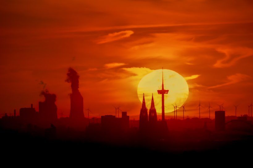 Sunset with silhouettes of towers and buildings in front of orange sky.