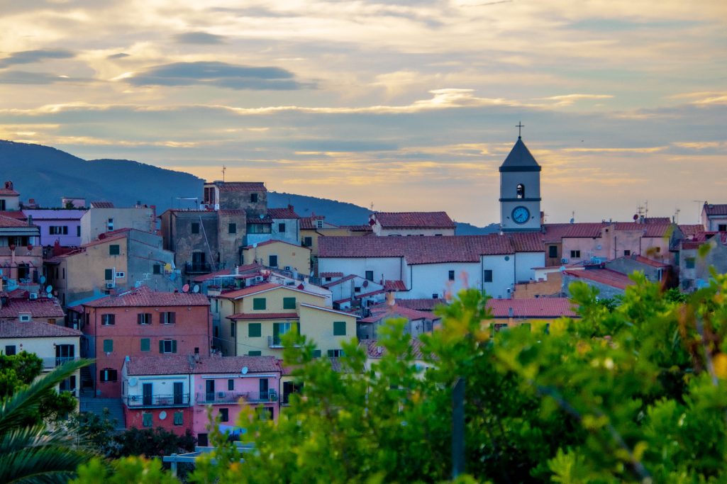 Colorful houses with church tower in front of rolling hills and cloudy sky.