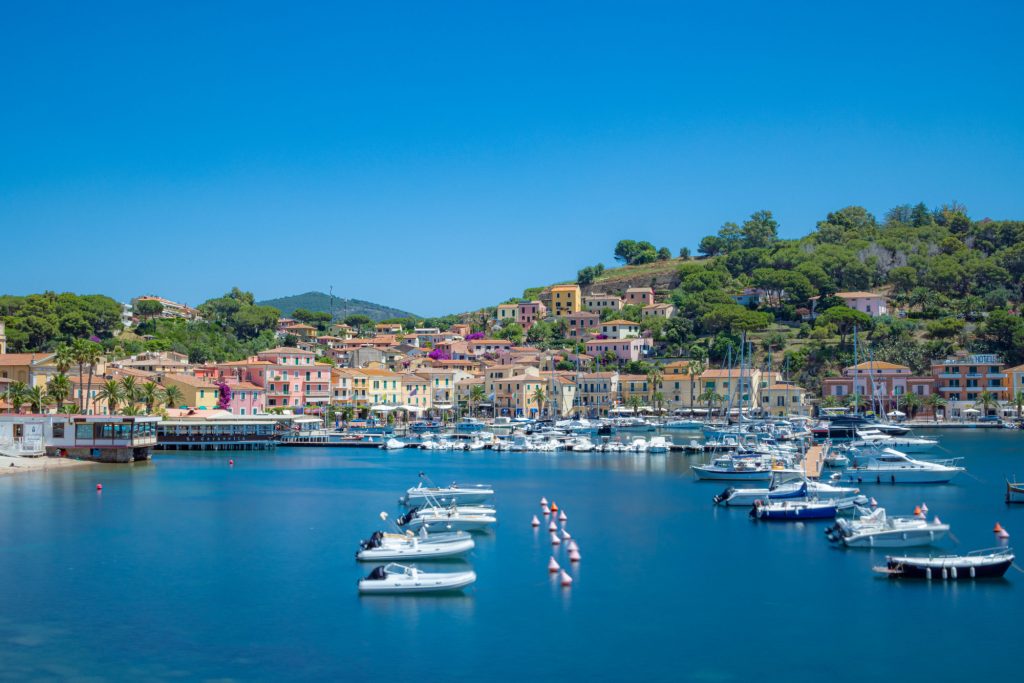 Harbour with many boats, surrounded by colorful houses and green landscape.