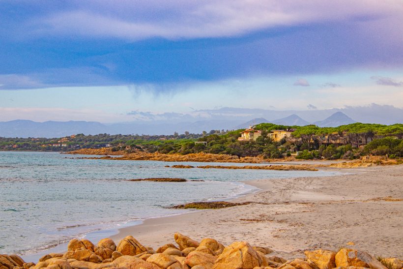 Beach landscape with rolling waves, rocks and wooded hills in the background.