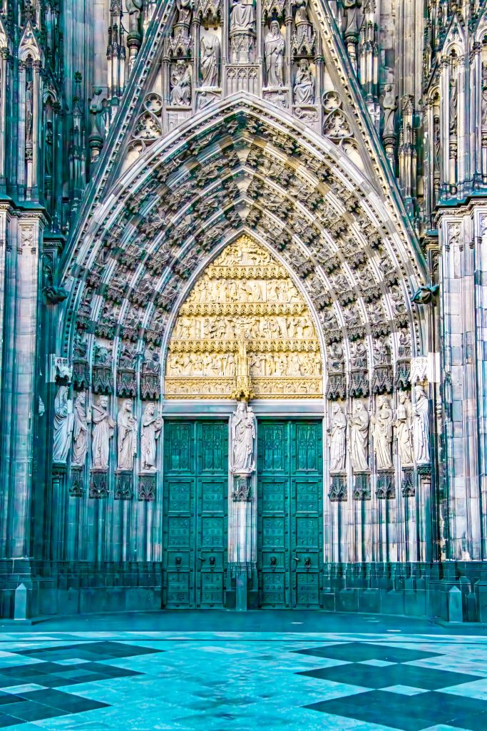 Große Eingangstür einer Kathedrale mit kunstvollem Steinmetzwerk und geometrischem Muster.