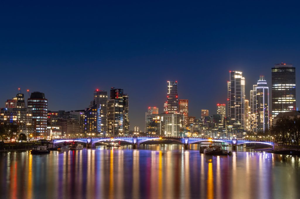 Blick auf die beleuchtete Skyline von London bei Nacht mit reflektierendem Wasser.