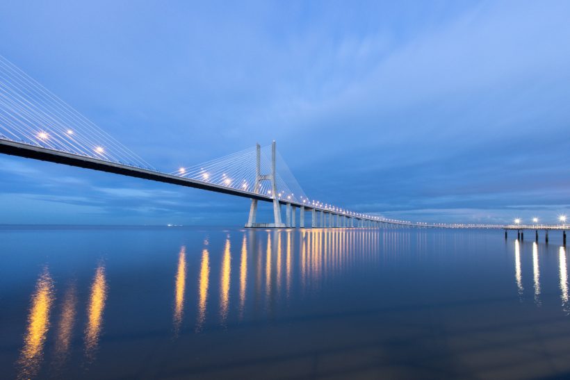 Stilvolle Brücke bei Dämmerung, reflektiert im ruhigen Wasser.