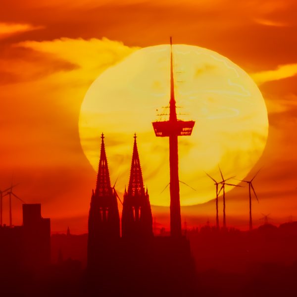 Sunset over Cologne Cathedral with silhouettes of church towers and a TV tower.