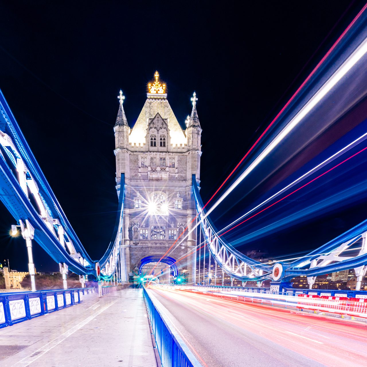 The Tower Bridge at night with light trails of vehicles in the foreground.