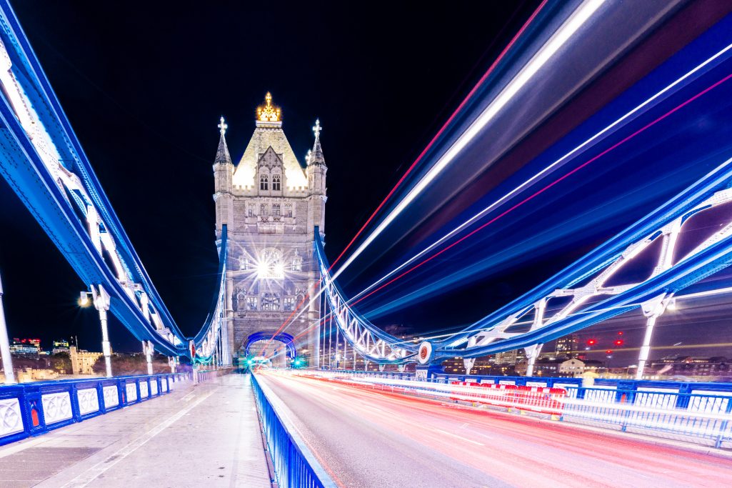 Turm der Tower Bridge bei Nacht, beleuchtet mit bunten Lichtern und Lichtstreifen.