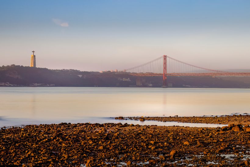 Blick auf die Brücke und einen Leuchtturm am Wasser bei Sonnenaufgang.