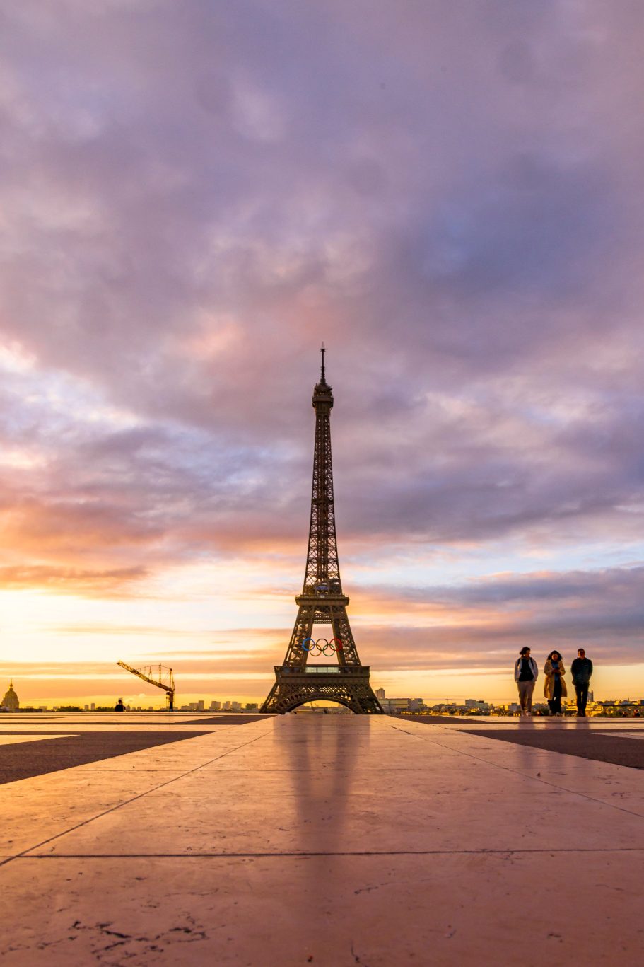 Eiffelturm bei Sonnenaufgang mit Silhouetten von drei Personen im Vordergrund.