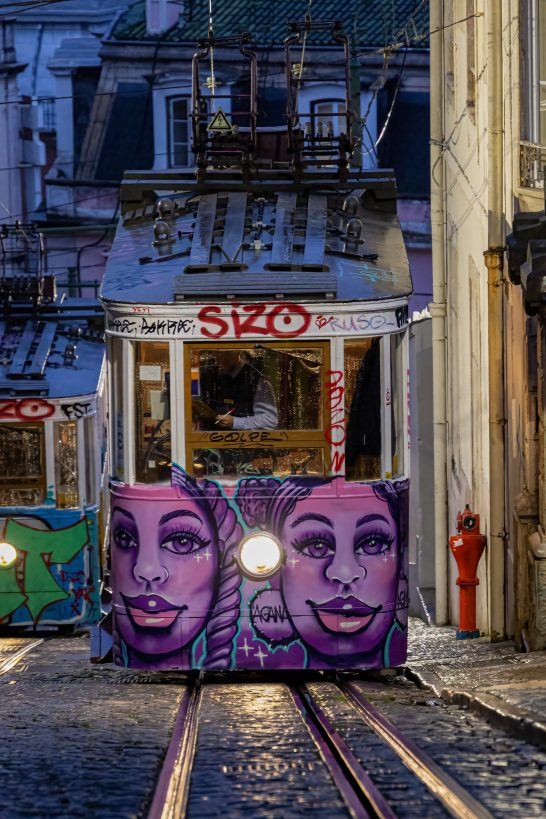 Colorful tram with graffiti faces in an urban setting at night.