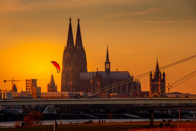 Kölner Dom silhouettiert vor einem Sonnenuntergang mit einem Gleitschirmflieger.