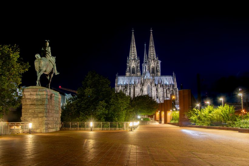 Night view of the cathedral with two towers, surrounded by trees and an equestrian monument.