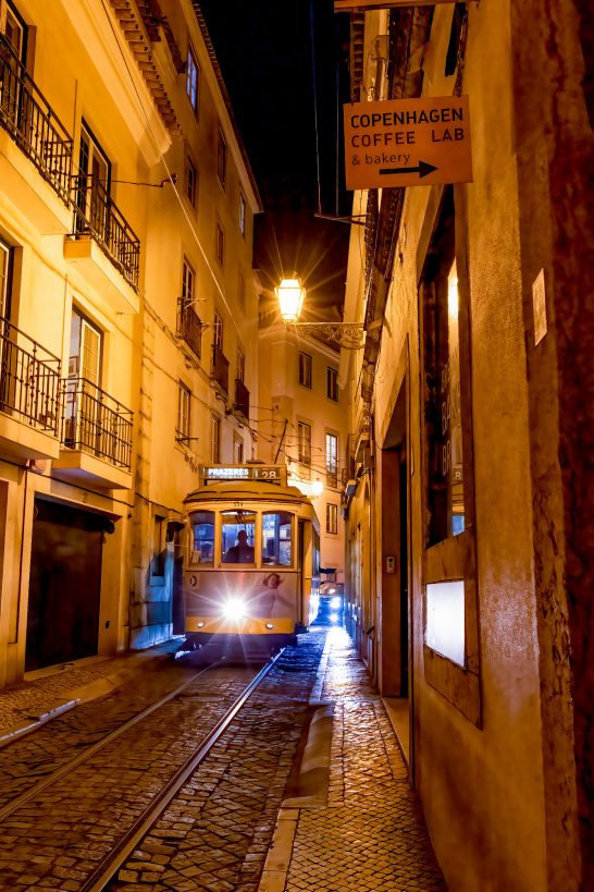 A tram runs through narrow, illuminated alleys in a city at night.