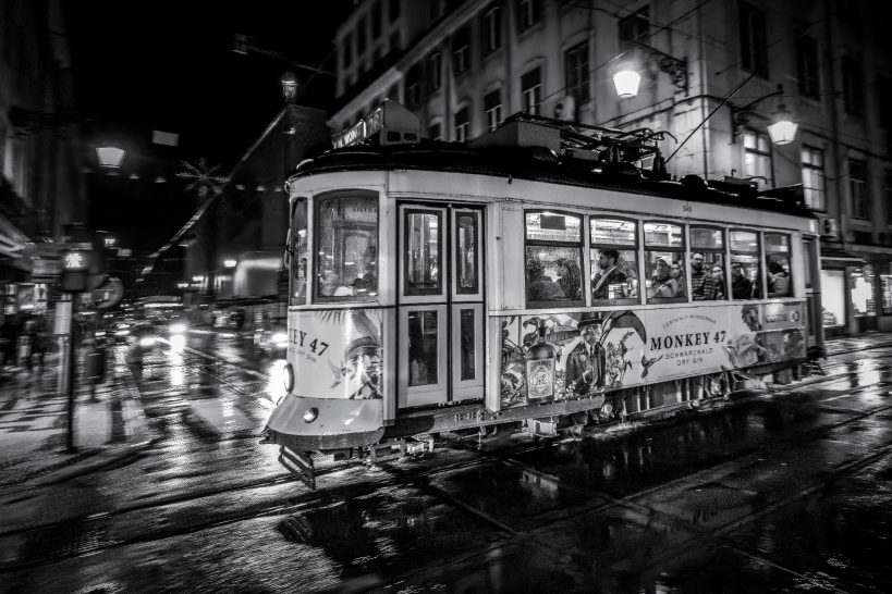 Black and white tram in a busy city at night, wet streets.