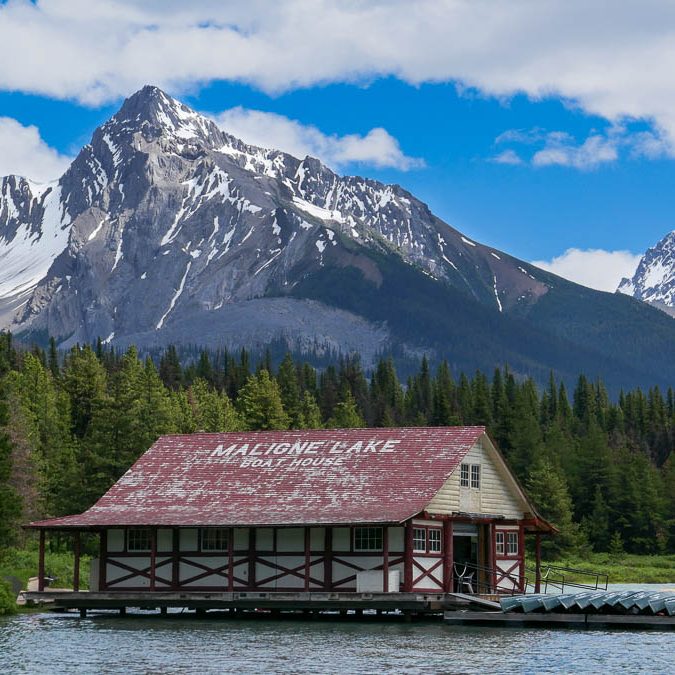 Holzhütte am Ufer eines Sees, umgeben von majestätischen Bergen und klarem Himmel.