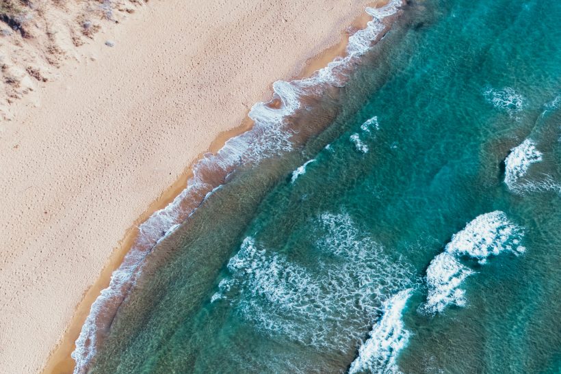 Strand mit sanften Wellen und klarem blauem Wasser, von oben betrachtet.