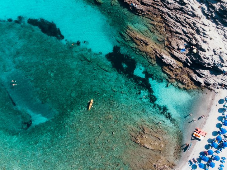 Crystal clear water with bathers and umbrellas on the beach.