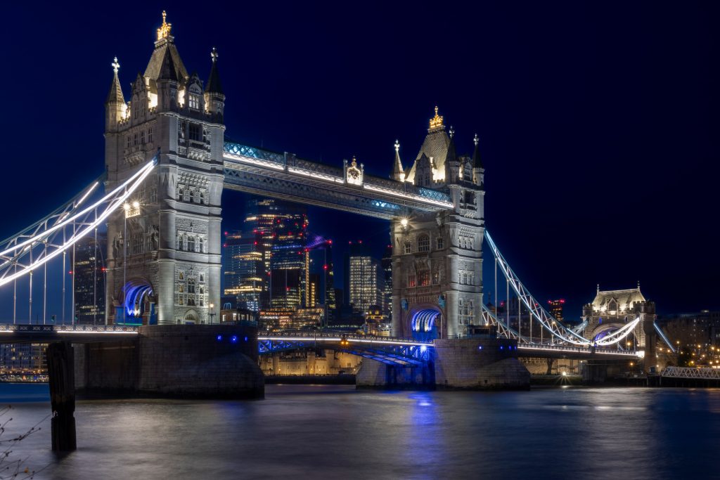 Die Tower Bridge bei Nacht mit beleuchteten Türmen und reflektierendem Wasser.