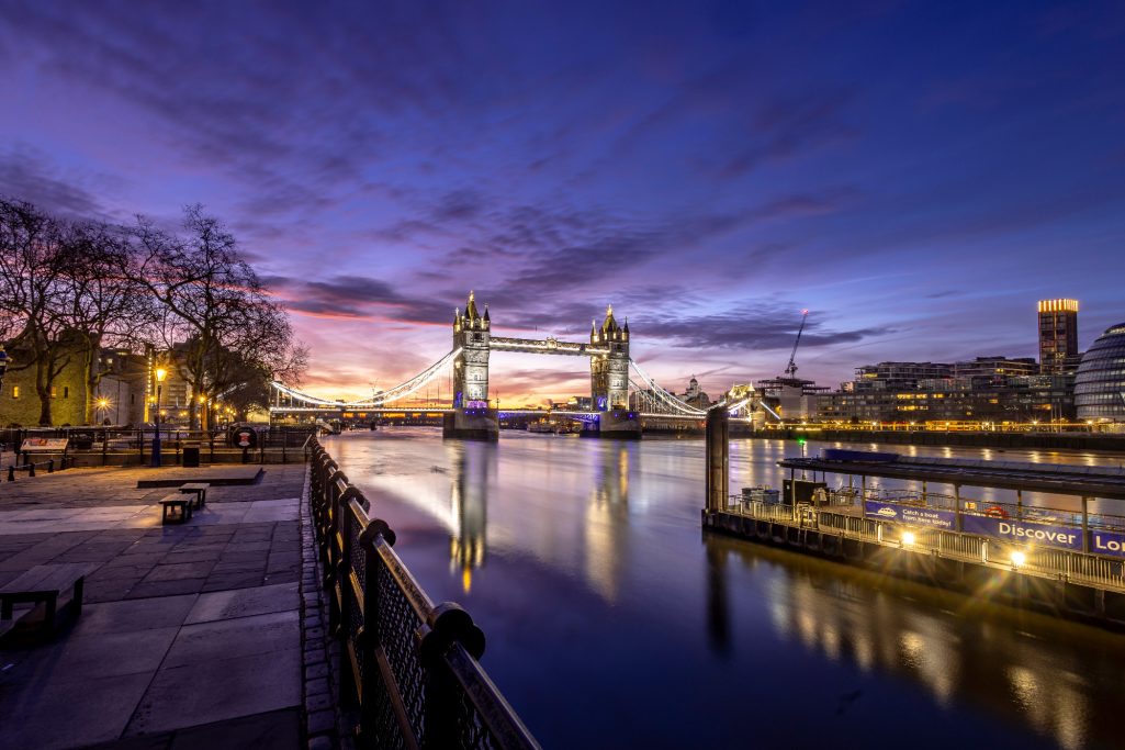 The Tower Bridge in London at sunrise, reflected in the calm water.