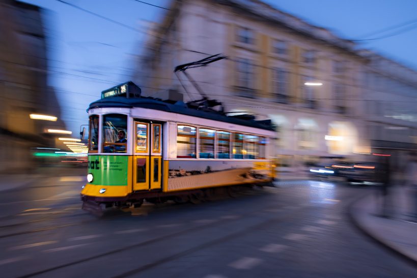 Colourful tram runs at dusk through a lively city street.