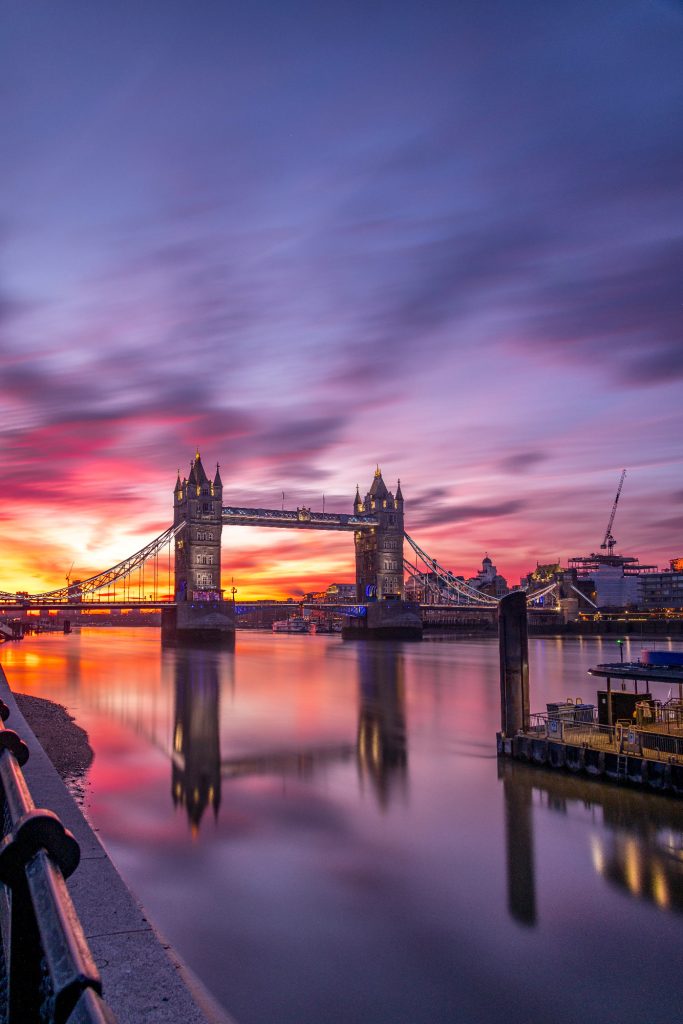 Tower Bridge at sunrise with reflective water and colorful sky.