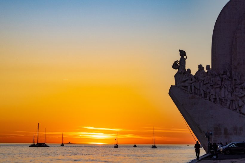 Silhouette of a monument in front of a stunning sunset by the sea.