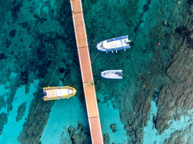 Harbour with several boats and a wooden bridge over clear, turquoise waters.