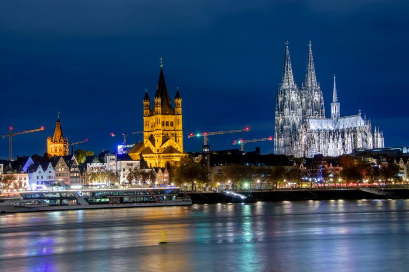 Kölner Skyline bei Nacht mit beleuchtetem Dom und historischem Gebäude.