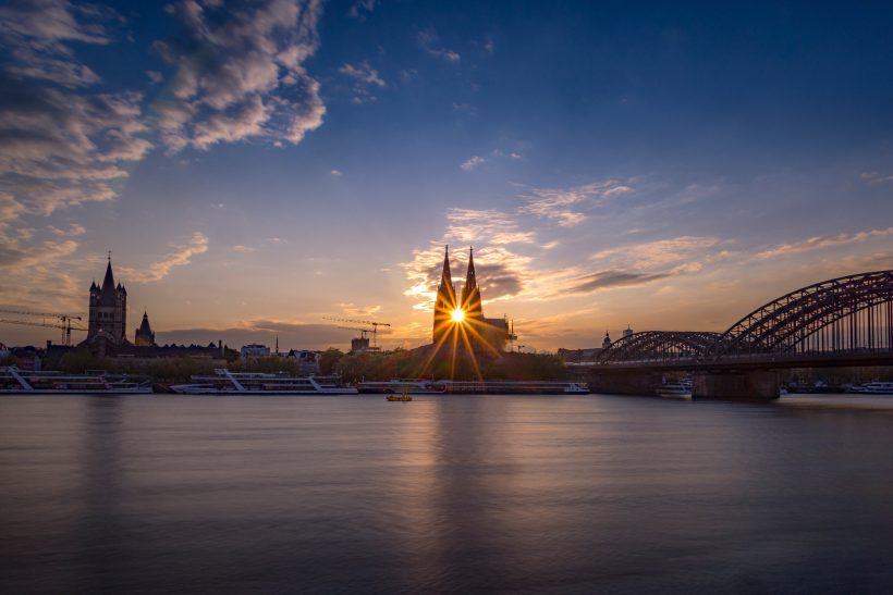 Sonnenuntergang über dem Kölner Dom und der Hohenzollernbrücke am Rheinufer.