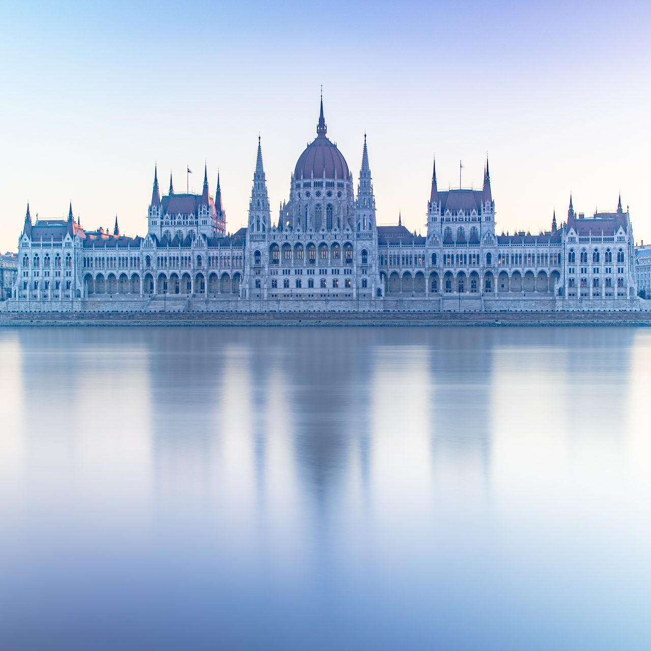 Ungarisches Parlament am Donauufer bei Sonnenaufgang, reflektiert im Wasser.