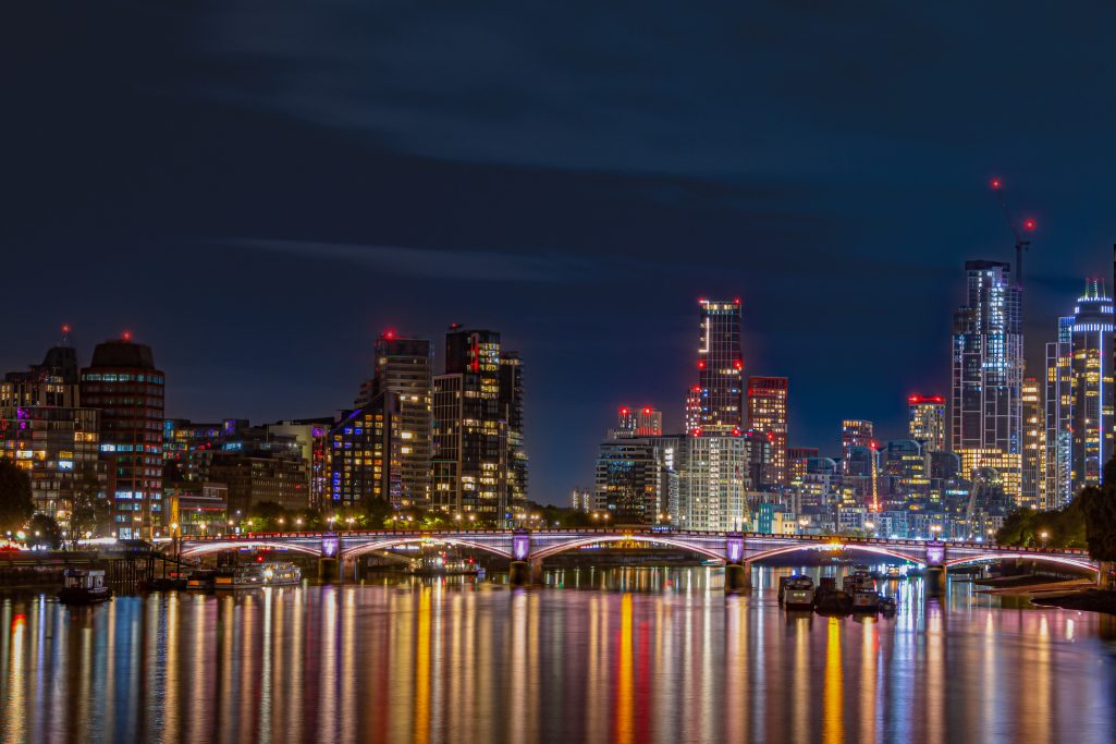 Night view of London with illuminated buildings and a reflective river.