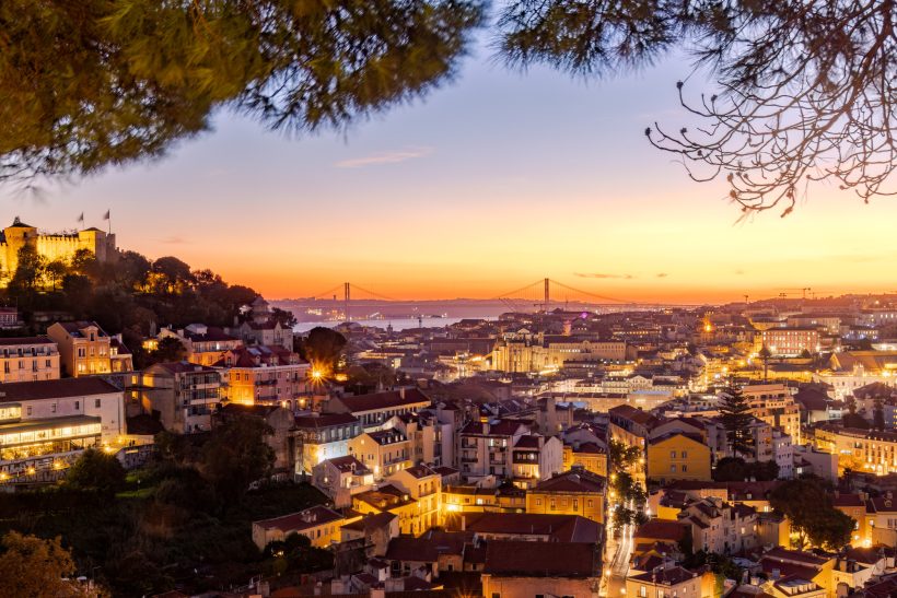 Panoramic views of Lisbon at sunset, with illuminated buildings and sky in warm tones.